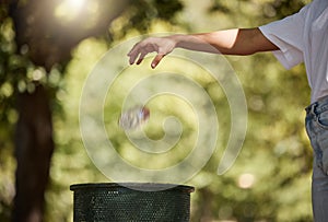 Closeup shot of a woman throwing her plastic cooldrink bottle into a bin outside in a park. The planet is our home