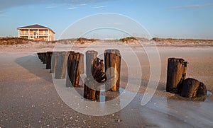 Closeup shot of wooden beach posts and a building on the background under the blue sky