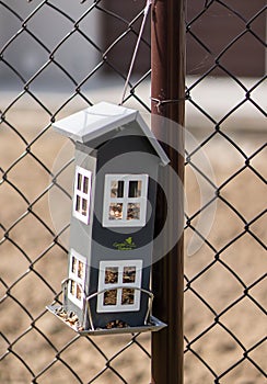 Closeup shot of wooden house-shaped bird feeding box hanging on a grid fence