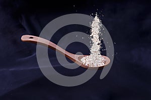 Closeup shot of a wooden spoon with pouring spices on a blue cloth background