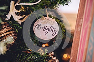 Closeup shot of a wooden toy with a word & x22;Almighty& x22; on a decorated Christmas tree