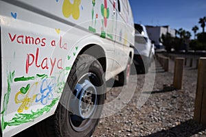 Closeup shot of "vamos a la playa" writing and colorful flower drawings on white van on sunny day