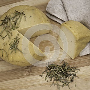 Closeup shot of yellow caciotta cheese with herbs on a striped wooden cutting board