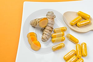 Closeup shot of yellow Curcuma root and pills with a wooden spoon on orange background