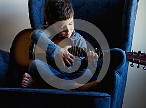 Closeup shot of a young boy learning to play guitar at home