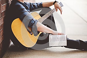 Closeup shot of a young male sitting with a book and a guitar in hands
