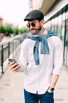 Closeup shot of young man messaging on smartphone. Happy smiling businessamn looking at smart phone leaning against a urban scene