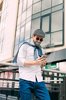 Closeup shot of young man messaging on smartphone. Happy smiling businessamn looking at smart phone leaning against a urban scene