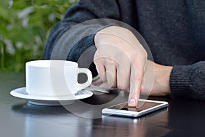 young man using a cellphone and drinking a coffee while sitting in a cafe