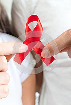 Closeup shot of a young man and woman holding a red ribbon - world AIDS day concept