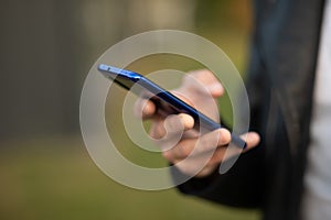 Closeup shot of an young modern man holding mobile phone in hand, blurred background