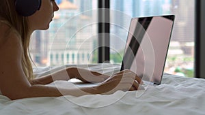 Closeup shot of a young woman freelancer lying on a bed listens to the music using a wireless headphones and working on