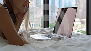 Closeup shot of a young woman lying on a bed listens to the music on her laptop using a wireless headphones when hears