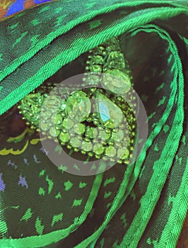 Closeup shows heart shape green rhinestone pin broach encircled with scarf fabric showing jewelry in macro size.