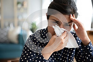 Closeup sick indian woman blowing her nose into paper napkin