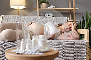 Closeup of sick pregnant woman lying on sofa at home with big variety of pills on background unhealthy female suffering flu and