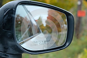 Closeup of the side mirror of car with the blur reflection of autumn trees