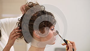 Closeup side view of elegance young woman getting makeup from make up artist in beauty studio. Hairstylist doing stylish
