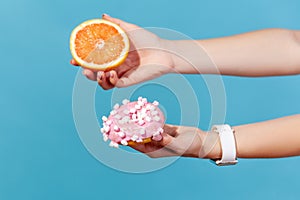 Closeup side view female hands holding sweet sugary donut and fresh grapefruit, choosing between healthy fruit vs junk food, carbs
