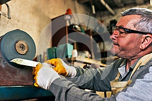 Closeup side view image of adult man manufacturing in his workshop. Worker man sharpens the knife in the repair shop