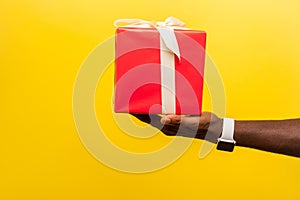 Closeup side view of male hand with wristwatches holding out red gift box. isolated on yellow background