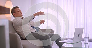 Closeup side view portrait of adult tired caucasian businessman using laptop sitting laidback on couch in apartment