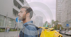 Closeup side view portrait of bearded caucasian delivery man with backpack walking on street in city outdoors with