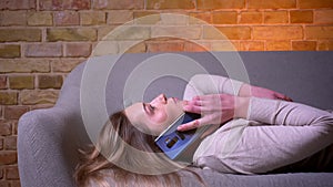 Closeup side view portrait of young attractive caucasian brunette female having a phone call lying laidback on the couch