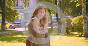 Closeup side view portrait of young cute caucasian female looking at camera drinking coffee smiling happily standing in