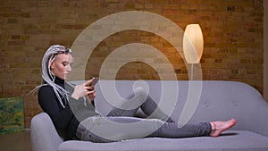 Closeup side view shoot of young attractive caucasian hipster female using the phone sitting laidback on the couch