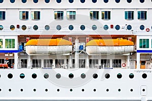 Closeup side view of a white passenger cruise ship with many round cabin windows and two lifeboats.