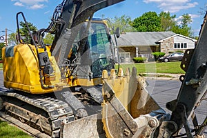 Closeup side view of a yellow heavy equipment excavator parked on the side of a residential street in front of a house