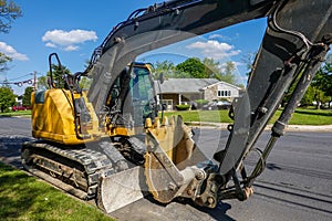 Closeup side view of a yellow heavy equipment excavator parked on the side of a residential street in front of a house