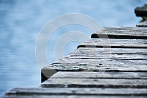 Closeup of the side of a wooden pier running diagonally across the frame with the lake visible in the background.