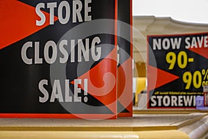 Closeup of signs for a store closing bankruptcy sale on top of a display case. Signs indicate 90% off.
