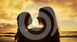 Closeup silhouette of mother and daughter standing on the beach at sunset. Backlit young woman and girl child smiling