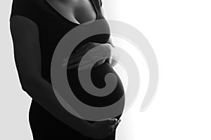 Closeup of silhouette pregnant woman in black dress with hands on belly on white background