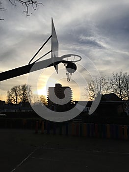 Closeup of silhouettes of basketball basket, buildings and trees at sunrise