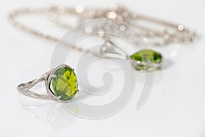 Closeup silver ring and pendant with peridot on white acrylic desk.