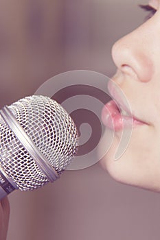 Closeup of singing caucasian child girl. Young girl emotionally sings into the microphone, holding it with hand.