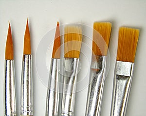 Closeup of six brushes of different shapes on white background