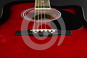 Closeup of a six stringed red acoustic guitar, from bridge side. Music entertainment background