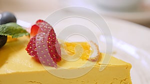 closeup of a slice of raw mango passionfruit cake garnished with strawberries and blueberries