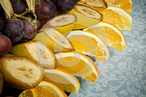 closeup sliced bananas, oranges and grapes on big plate