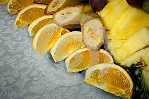 Closeup sliced bananas, oranges and pineapples on big plate