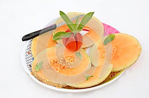 Closeup sliced ripe orange muskmelon with red tomato mint and knife isolated on white background