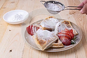Closeup of sliced waffles with fresh strawberries and sprinkled with powdered sugar