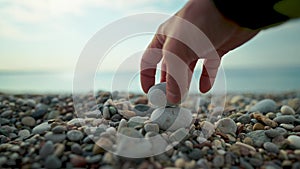 closeup slow motion man's hand tries to build a stone piramida with pebble on sea beach. stone has no balance and