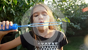 Closeup slow motion video of cute smiling girl blowing soap bubbles in camera