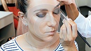 Closeup slow motion video of female visagiste applying makeup on models face in professional makeup studio